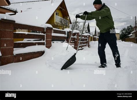 Guy In Jacket Hat And Gloves Shovels Snow In Front Of House After