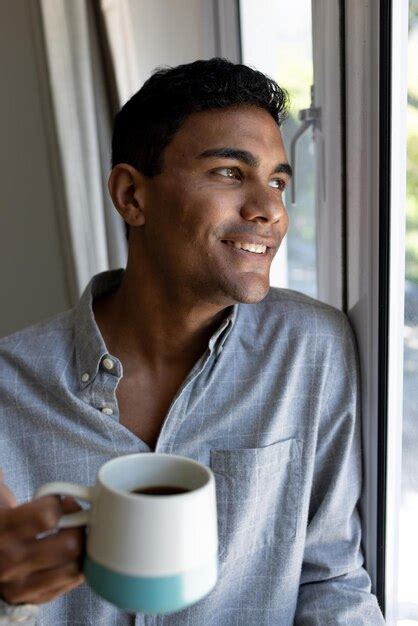 Premium Photo Happy Biracial Man Holding Mug Looking Through Window