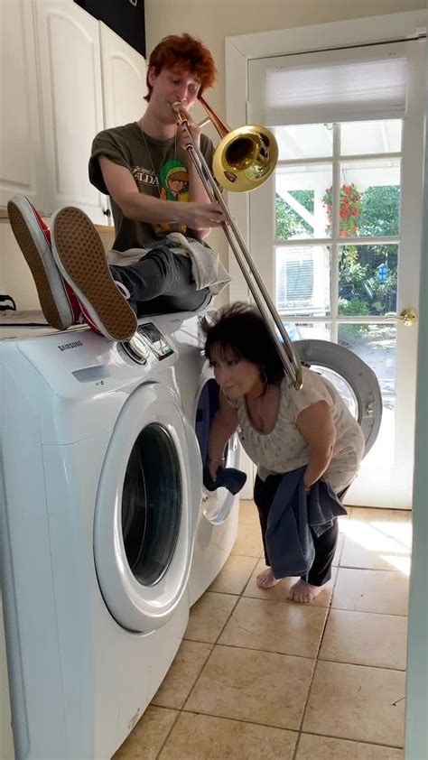 a woman is playing the trumpet in front of a washing machine while another person looks on