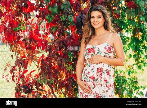 Outdoor Portrait Of Beautiful Pregnant Woman Wearing Floral Dress