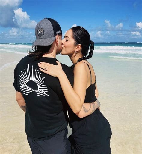 A Man And Woman Kissing On The Beach While Wearing Matching Shirts That