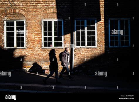 Man Passing By An Old Building With Brick Wall And White Windows In