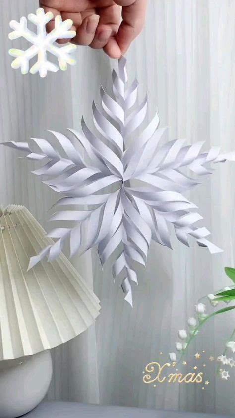 A Person Holding A Paper Snowflake In Their Hand Next To A Table Lamp