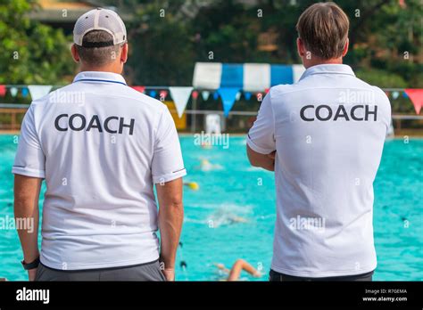 Back View Of Swimming Coaches Wearing Coach Shirt Working Together At