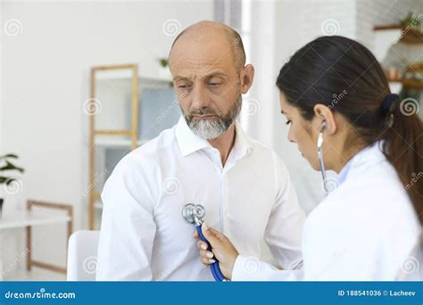 Young Female Cardiologist Listening To Senior Man`s Heartbeat At Clinic Doctor Examining