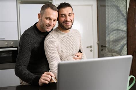 Premium Photo Smiling Gay Men Using Laptop While Embracing At Home