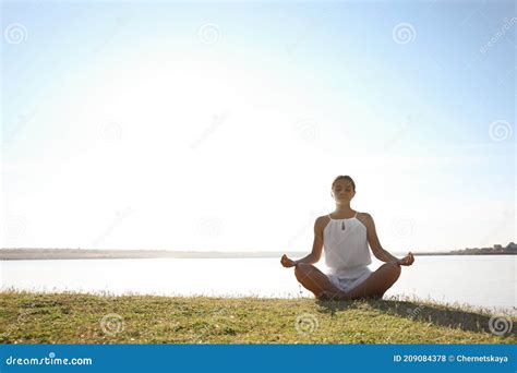 Young Woman Meditating Near River At Sunset Space For Text Nature