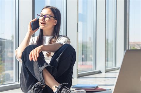 Uma jovem de óculos está falando em um smartphone perto da janela