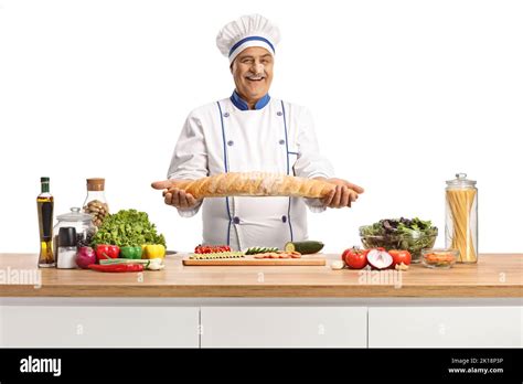 Mature Male Chef Holding A Baguette Bread Behind A Kitceh Counter