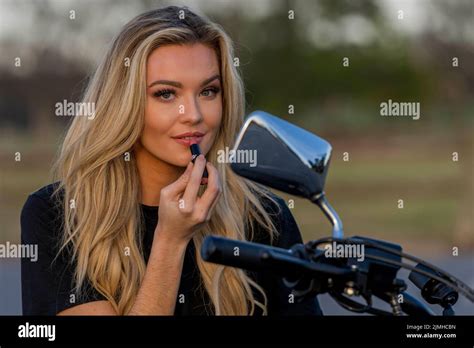 A Lovely Blonde Model Enjoys The Outdoor Weather While Posing With Her Motorcycle Stock Photo