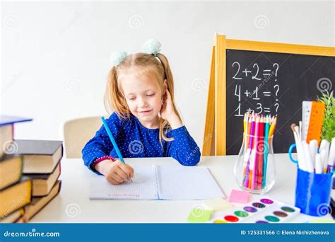 Happy Cute Industrious Child Is Sitting At A Desk Indoors Stock Photo