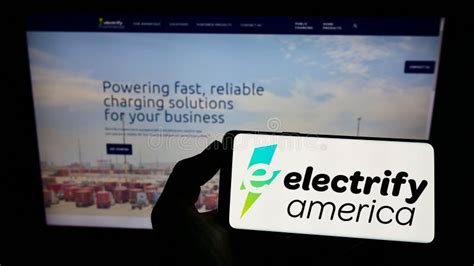 Person Holding Smartphone With Logo Of Us Ev Charging Company Electrify