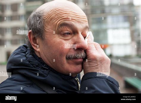 An elderly man with a mustache and bald head wipes tears in his eyes ...