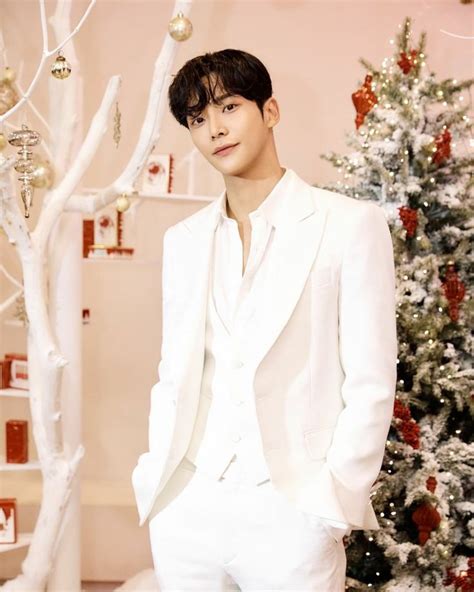 A Man In A White Suit Standing Next To A Christmas Tree