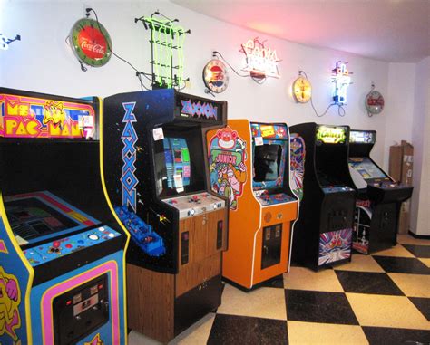 Several Arcade Machines Lined Up In A Room With Checkered Flooring And Neon Signs On The Walls