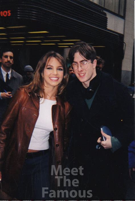 A Man And Woman Standing Next To Each Other In Front Of A Sign That