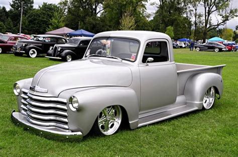 An Old Silver Truck Parked On Top Of A Lush Green Field Next To Other