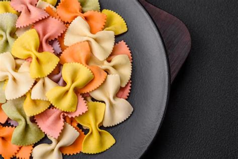 Pasta farfalle cruda en diferentes colores sobre un fondo de hormigón ...