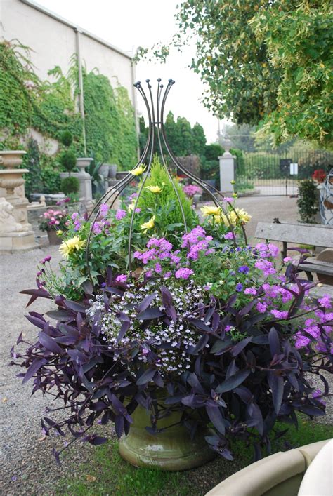 Purple And Yellow Flowers Are In A Green Vase On The Ground Near A Park