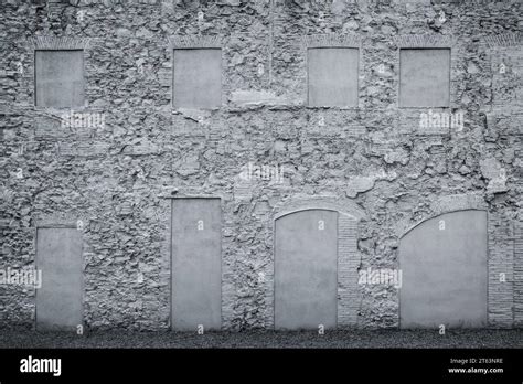 An Old Textured Brick Wall With Blocked Windows And Arched Doorways In