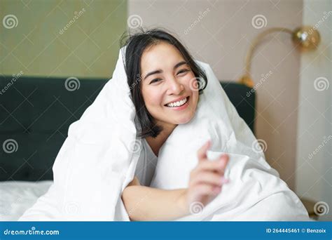 Beautiful Asian Woman Sitting On Bed Covered With White Duvet Smiling