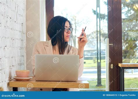 Beautiful Brunette Woman Working In A Cafe At A Laptop And Near A Cup Of Fresh Aromatic Coffee