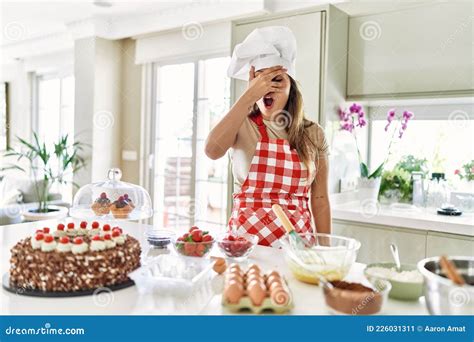 Beautiful Young Brunette Pastry Chef Woman Cooking Pastries At The Kitchen Peeking In Shock