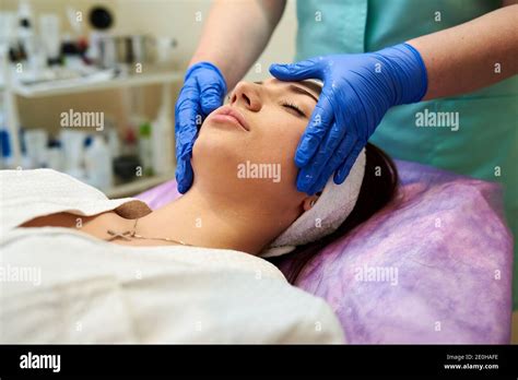 Cosmetologist Masseuse Cleaning Woman Face At Spa In Cosmetic Cabinet