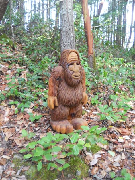 A Statue Of A Bigfoot Sitting In The Woods Next To A Tree Trunk And