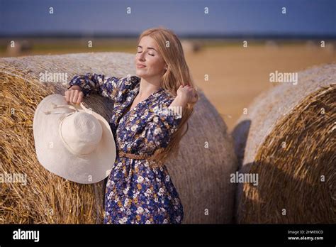 Une jeune fille blonde aux cheveux longs dans un chapeau blanc se repose et pose près des gerbes