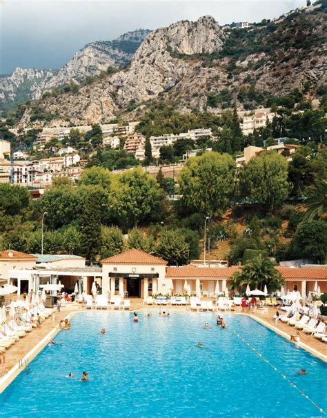 An Outdoor Swimming Pool With Lounge Chairs And Umbrellas In Front Of