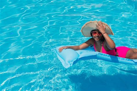 Sonriente joven africana en bikini con sombrero de paja relajándose en