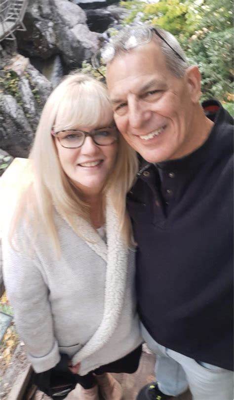 An Older Man And Woman Are Posing For A Photo In Front Of Some Water