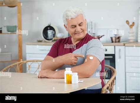 Diabetic Mature Man With Glucose Sensor At Table In Kitchen Stock Photo