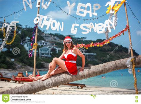 Cute Blonde Woman In Red Dress Sunglasses And Santa Hat Sitting On Palm Tree At Exotic Tropical