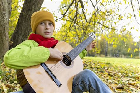 Chico toca la guitarra en el parque de otoño niño aprende a tocar la