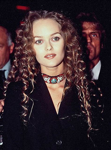 A Woman With Long Curly Hair Wearing A Collared Shirt And Black Jacket