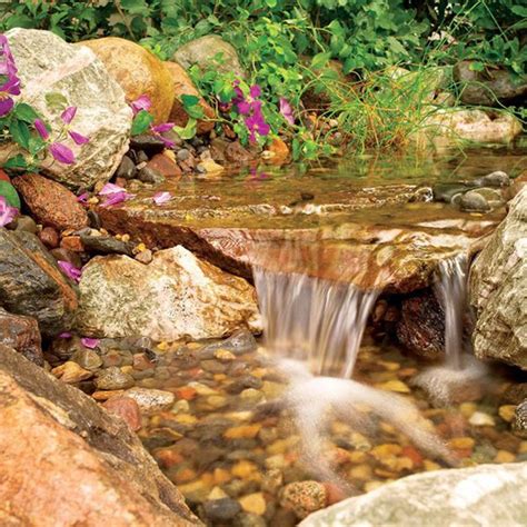 There Is A Small Waterfall In The Middle Of Some Rocks And Flowers On