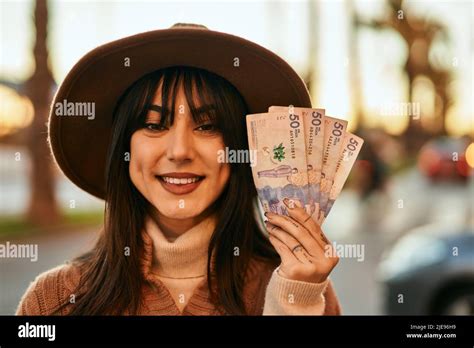 Brunette Woman Wearing Winter Hat Smiling Holding Colombian Pesos Banknotes Outdoors At The City