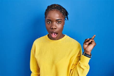 Beautiful Black Woman Standing Over Blue Background Surprised Pointing With Finger To The Side