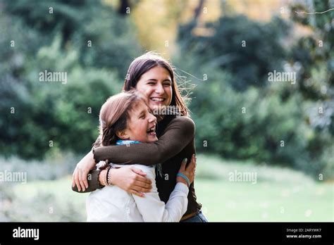 Smiling Sisters Embracing By Bush Stock Photo Alamy