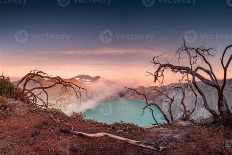 árbol seco en el cráter del volcán activo con lago turquesa al amanecer