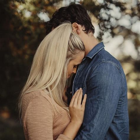 A Man And Woman Embracing Each Other In Front Of Trees With Their Heads Close Together