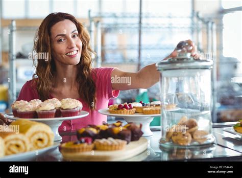 Pretty Brunette Smiling At Camera Behind Plates Of Pastries Stock Photo