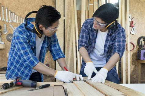 Two Young Man As Carpenter Apprentices Work On The Circular Saw In The