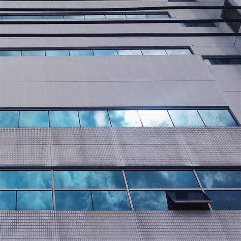 A Tall Building With Many Windows And Sky Reflected In It