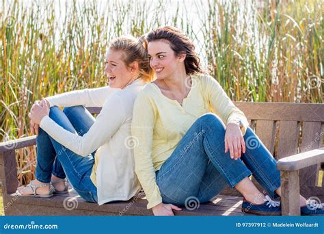 Two Happy Friends Sitting On Park Bench Talking And Interacting Stock