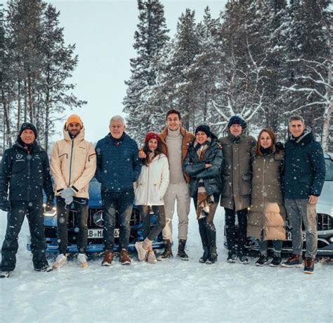 a group of people standing next to each other in front of a car on snow ...