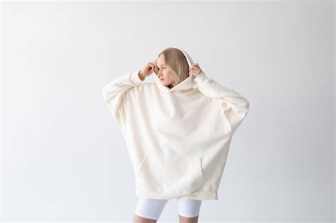 Schöne blonde Frau posiert in weißem Hoodie und Leggings gegen weißen Hintergrund Kostenlose Foto
