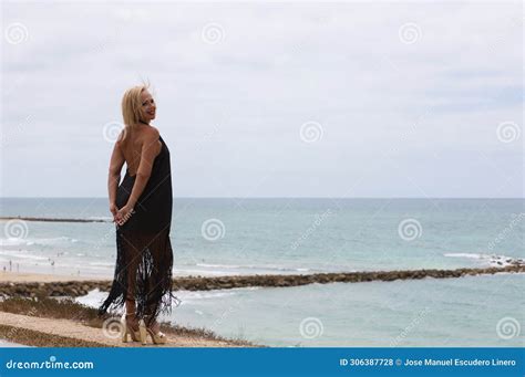 Mature Blonde And Beautiful Woman Wears An Elegant Black Dress And Poses For The Pictures Happy